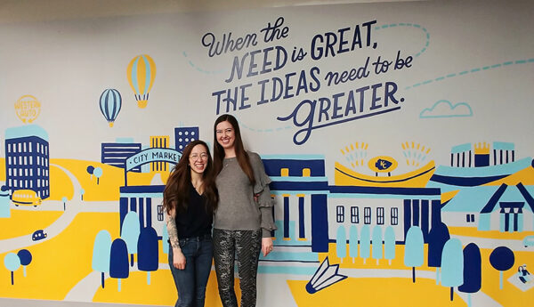 Employees in front of a wall mural that reads "When the need is great, the ideas need to be greater."