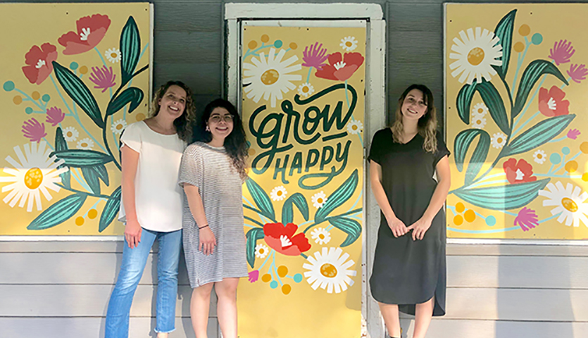 Three Hallmark employees in front of a wall mural with flowers that reads "Grow Happy."